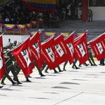 Miembros de la Fuerza Armada de Venezuela durante el primer aniversario de la muerte de Hugo Chávez portando banderas rojas con una silueta de sus ojos junto con la frase «Chávez vive, la lucha sigue».